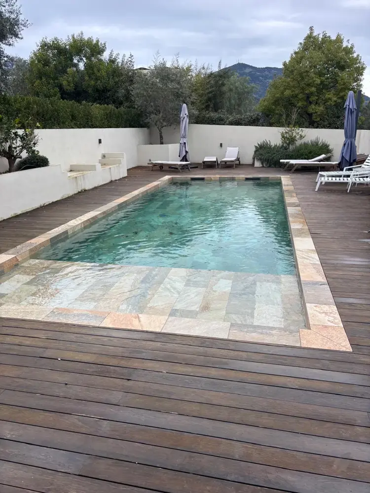 Piscine en pierre bordée d’une terrasse en bois, montagnes au loin